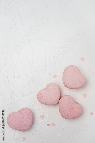 Pink heart-shaped macarons, decorated with small scattered hearts, flat laying on a white textured background, symbolizing romance, affection and sweet indulgence for special occasions