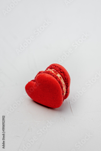 Red heart shaped macaron with cream filling resting on a textured white surface, symbolizing love, romance, and sweet indulgence for Valentine's Day celebrations and special moments