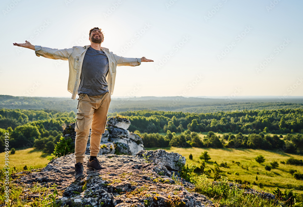 Naklejka premium Young man with outstretched arms standing on top of a rock in Jura Poland enjoying summer day
