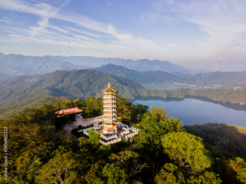 Aerial view of Ci En Pagoda rising above forested hills at Sun Moon Lake, Taiwan, with the blue lake and surrounding mountains in the background on a clear, sunny day.

