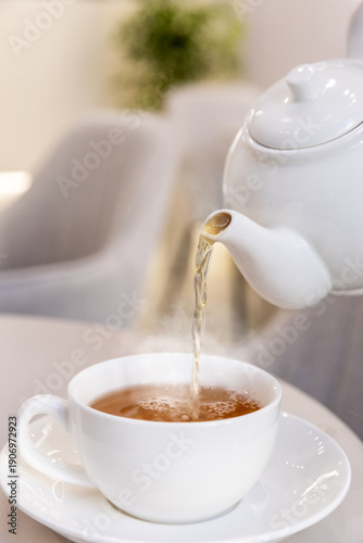 Tea is being poured from a teapot into a white cup on a table in a cafe