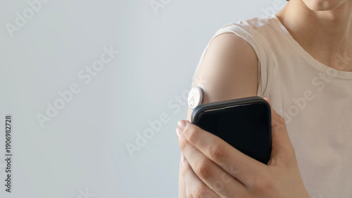 Close-up of young person using smartphone to scan continuous glucose monitor CGM sensor on their arm. Modern healthcare technology for diabetes management and blood sugar tracking