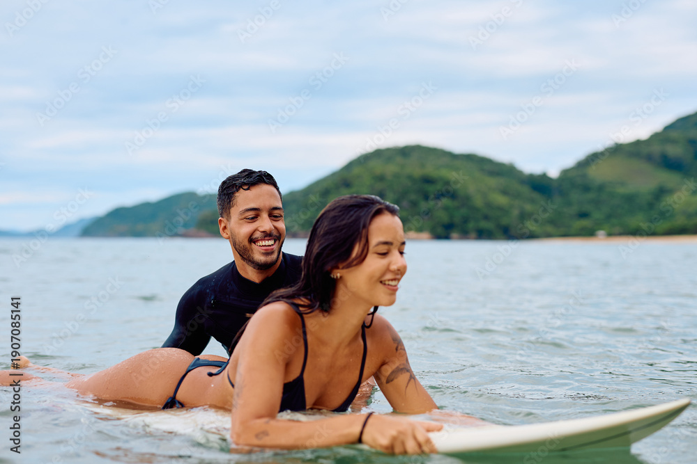 Obraz premium Young couple on a surfboard, smiling and learning to surf. Enjoying a fun summer activity on a beautiful day
