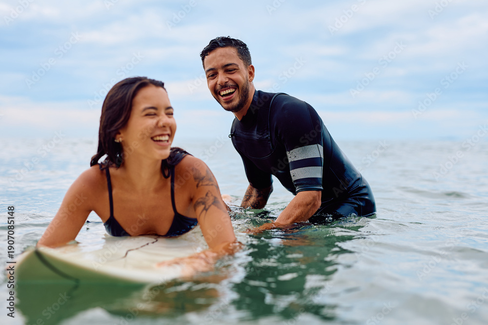 Obraz premium Surfing couple laughing, enjoying an active summer vacation, learning to surf and having fun together in the sea