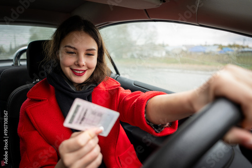 Konstfotografi A young, attractive girl sits in a car, joyfully holding her new driver's license, celebrating passing her driving test