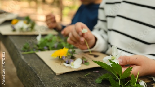 Konstfotografi Children's hands crafting nature art with wildflowers and green leaves on a wood