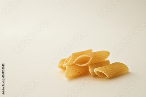 Fotografie Pile of dry penne rigate pasta tubes on a plain light background, close-up studi