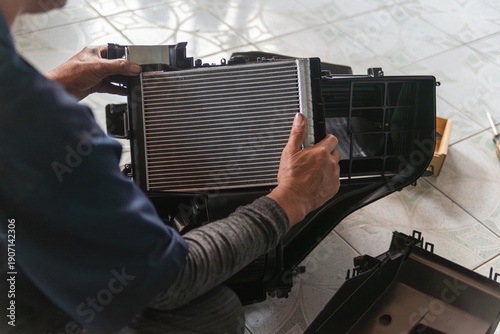 Close-up of a mechanic's hands assembling a new aluminum cooling coil into the car A/C housing unit during maintenance repair.