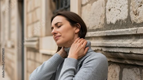 Woman relieves neck tension outdoors with stretching against stone wall