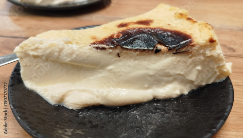 Porción de tarta de queso cremosa al estilo vasco con superficie tostada servida en plato negro