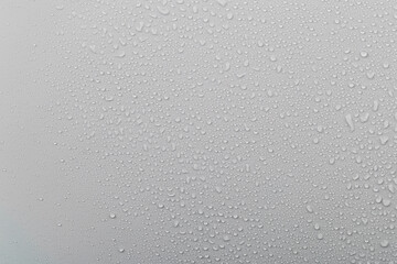 Water droplets on glass with a grey background create a textured surface during rainy weather in the afternoon light