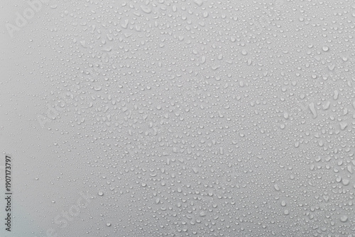 Water droplets on glass with a grey background create a textured surface during rainy weather in the afternoon light