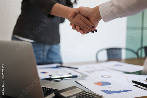 Billede på lærred Businesspeople shaking hands in the meeting over a desk with business documents and laptop for the start or culmination of a professional relationship or negotiation