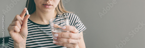Woman holding a white pill and glass of water to treat painful lip herpes virus.