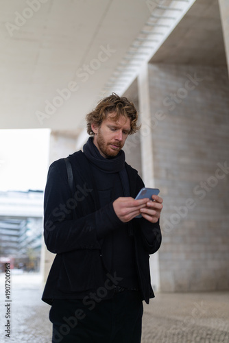 Foto Young man using smartphone communicating online in urban setting