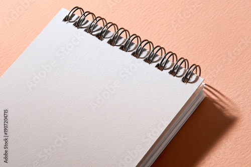 Close-up of a spiral-bound, blank notepad lying on a peach-colored textured surface