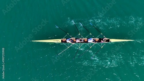 Aerial drone cinematic tracking video of team of athletes synchronous rowing in sport canoe in emerald calm lake