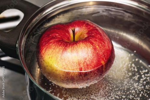 Obraz na plátně Red apple floating in boiling water inside metal pot closeup