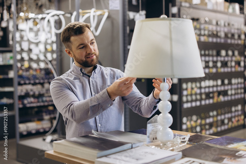 Принти на полотні Man shopping for home lighting, selecting a modern table lamp in a store, bright