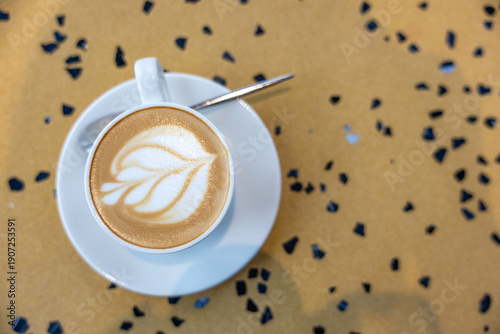 Top view of cappuccino with latte art in white cup on saucer with spoon.