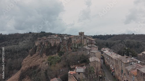 Aerial view of Calcata Vecchia, an ancient medieval village perched on a rocky cliff in Lazio, during a gloomy day. Historic stone houses surrounded by forest and dramatic landscape of a scenic view.
