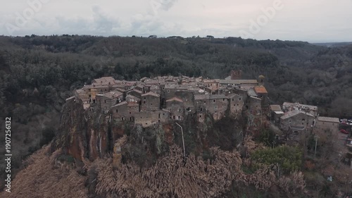 Aerial view of Calcata Vecchia, an ancient medieval village perched on a rocky cliff in Lazio, during a gloomy day. Historic stone houses surrounded by forest and dramatic landscape of a scenic view.

