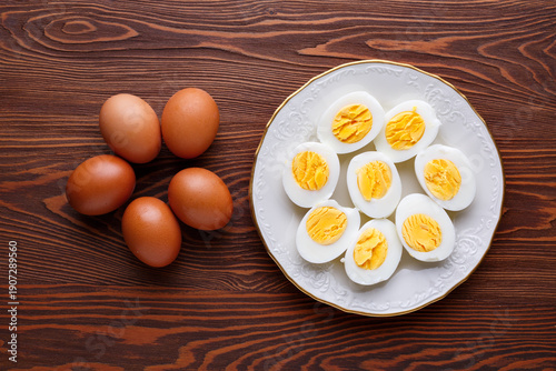 Fotografija Hard-boiled chicken eggs lie on a white plate on a dark wooden table