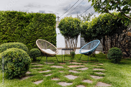 Cozy garden seating area with two outdoor lounge chairs, table, lawn and trimmed shrubs