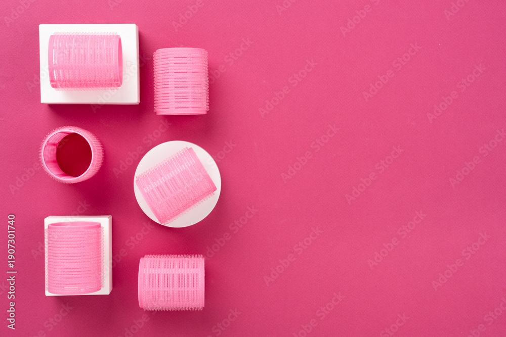 Obraz premium Pink hair curlers on color background, top view