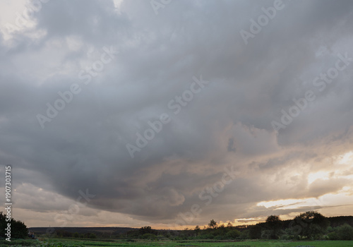Dramatic thunderous sunset sky with dark huge rain clouds over green forest