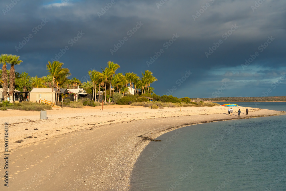 Obraz premium Romantic Monkey Mia beach at sunset with calm ocean waves and silhouetted coastal dunes backdrop