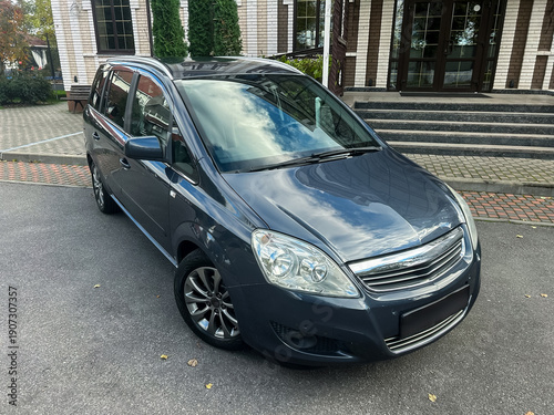 Fotografi Dark gray car parked in front of a modern building surrounded by greenery on a c