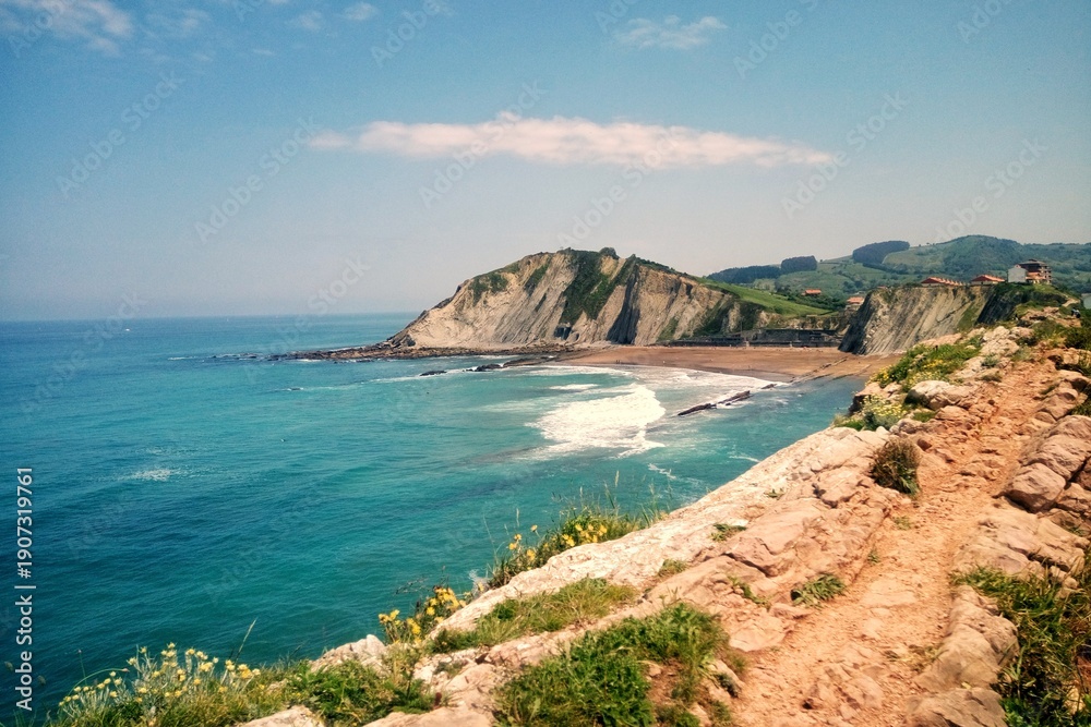 Naklejka premium Panoramic view of Itzurun beach with flysch geological formations and cliffs in Zumaia under a blue sky in Basque Country Spain. Coastal landscape of the Bay of Biscay in UNESCO Global Geopark area