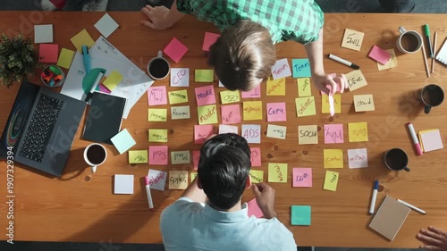 Top view of skilled business people discuss plan at meeting room while writing idea at sticky notes and stick at whiteboard. Group of diverse team working together to planning strategy. Convocation.