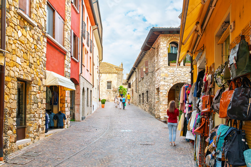 Bilde på lerret A picturesque and colorful cobblestone street of historic stone buildings full of shops in the historic medieval center of Sirmione, Italy, on the shores of Lake Garda