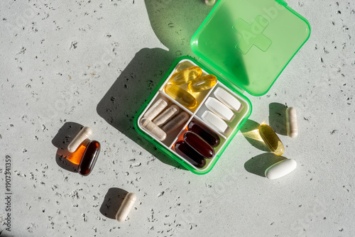 Various health supplements in a green container with some capsules on a light surface during daytime