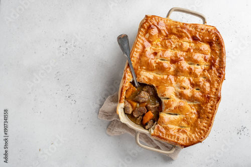 Warm beef and vegetable pie on a kitchen counter with a spoon resting in the filling and a piece removed