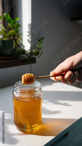 Honey Dripping from Wooden Dipper into Glass Jar in Natural Sunlight