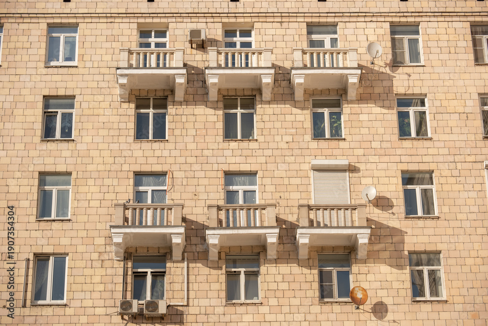 Fototapeta premium Residential building facade with windows, balconies, brick wall and sunlight shadows