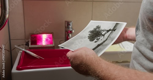 Darkroom lab worker reviewing finished photographic print after analog photo printing process