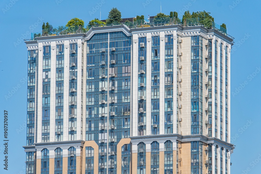 Obraz premium Multi-story residential building with classical architectural style, symmetrical facade, vertical windows, balconies, neutral color scheme, daytime lighting, elevated perspective, city backdrop