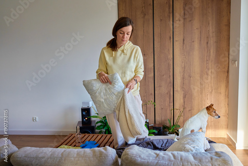 Cuadro en lienzo Woman standing in living room holding pillow and blanket while tidying sofa