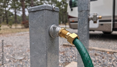 Medium shot capturing water hose attachment to a 50amp RV hookup pedestal emphasizing the faucet and hose fitting with the background campsite out of focus