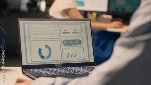 Fotografie Male office worker solving tasks independently on laptop at desk, reviewing visual data, charts and graphs