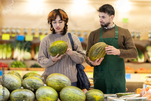 Tableau sur toile Polite young male seller offering melon to girl standing by product stand in gro