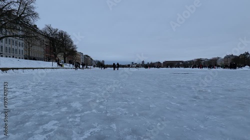 Many people walk on the ice in the middle of a canal in the city. The capital of Denmark. The city is surrounded by winter. Cold winter
