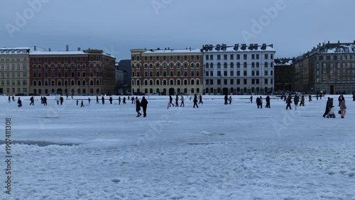 A view across a frozen canal of people on the ice. Many people walk on the ice. The capital of Denmark