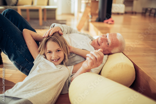 Fényképezés Grandfather and granddaughter relaxing on living room floor