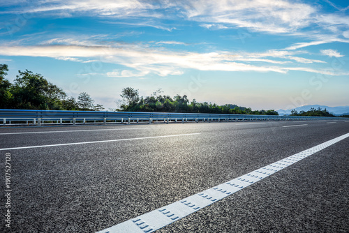 Foto Empty asphalt highway with white lines and metal guardrails under a blue sky wit