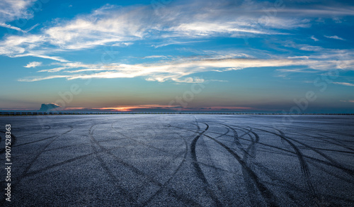Wide open asphalt race track featuring black tire burnout marks under a dramatic sunset sky